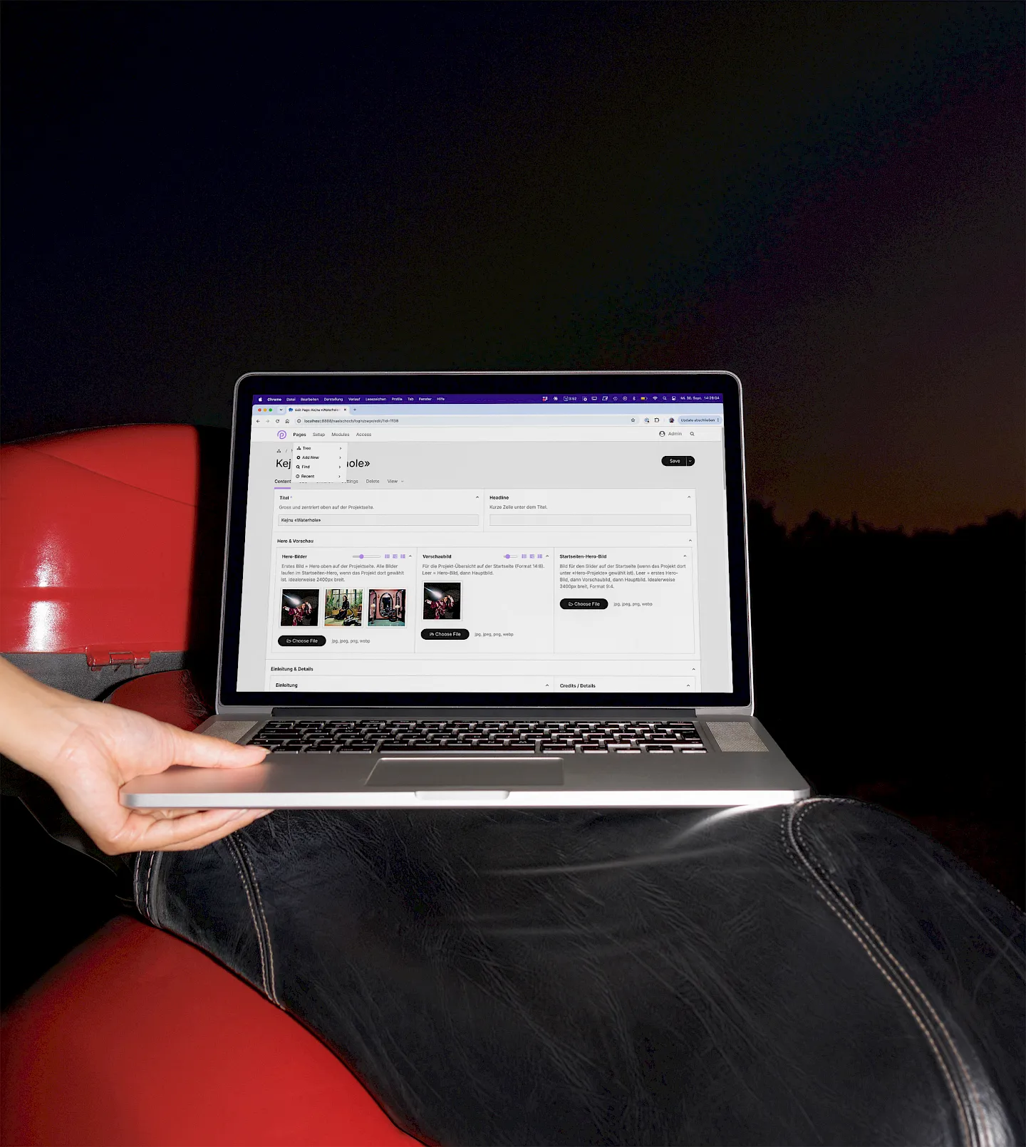 Hand hält Laptop mit ProcessWire-Backend auf rotem Ledersessel in dunkler Umgebung