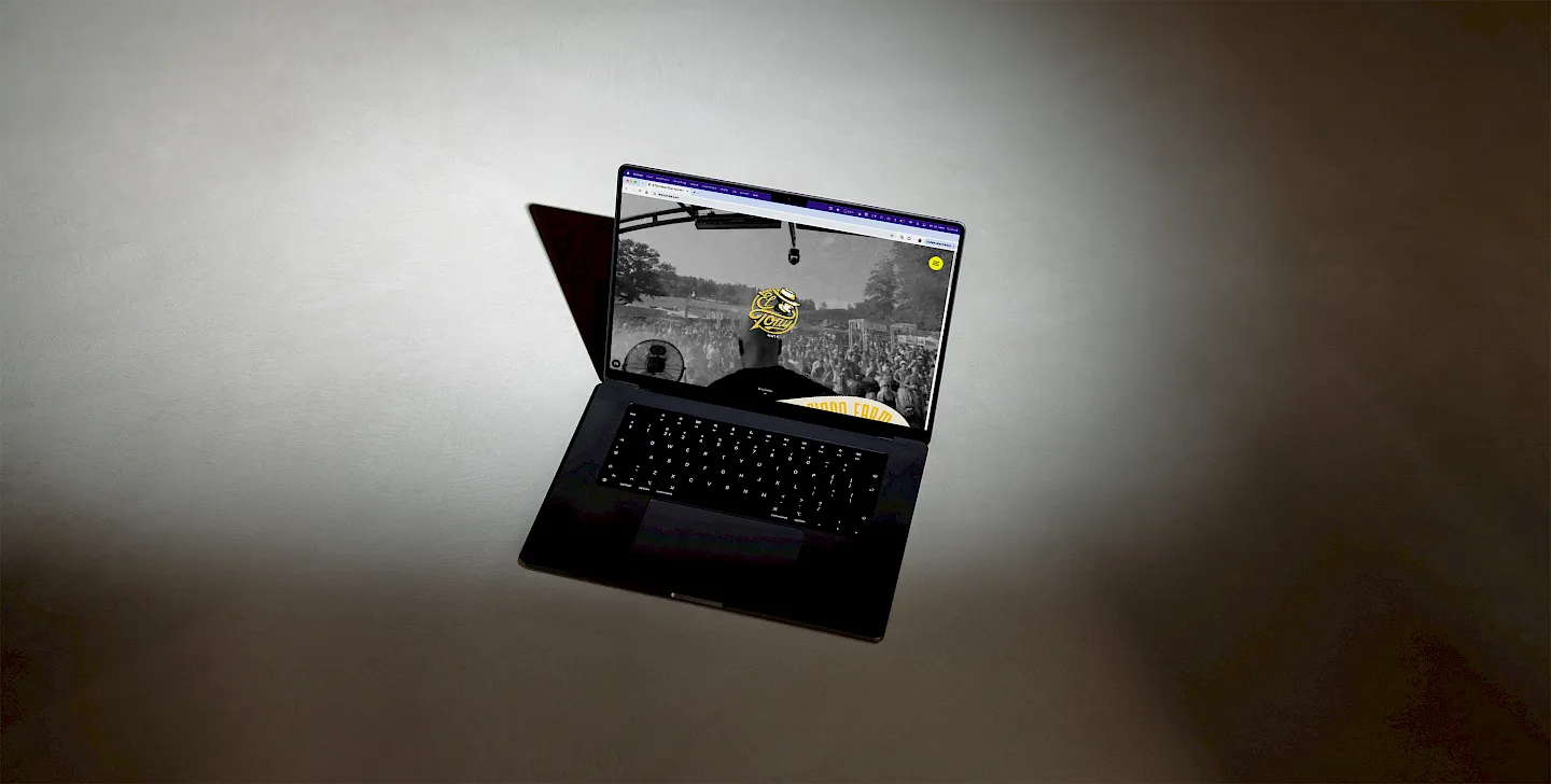 Laptop zeigt Webseiten-Screenshot mit Bühnenfoto und Mikrofon vor grauem Hintergrund