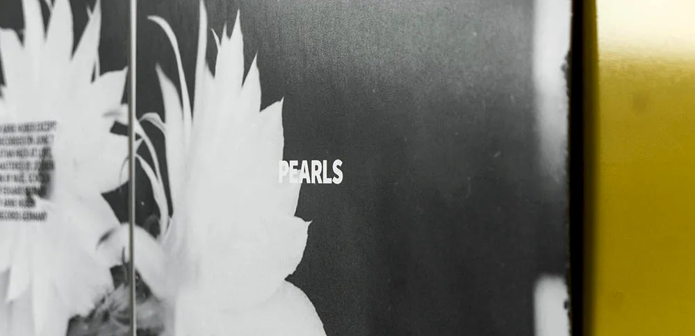 Close-up of the booklet featuring a floral motif, the word “Pearls,” and a yellow CD edge in the background